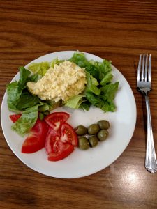 egg salad on bed of lettuce, tomato and green olives on the side