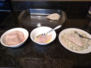 showing how to bread the chicken with bowls and plates of ingredients lined up on counter.