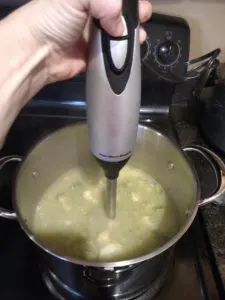 blending Creamy Broccoli Cauliflower Cheese Soup with hand blender to make creamy