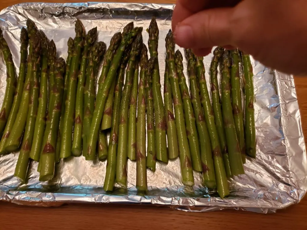 asparagus on baking sheet being sprinkled with seasonings