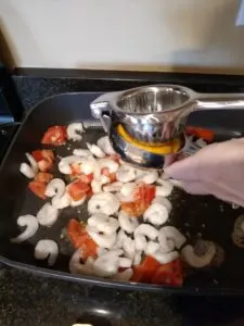 shrimp and tomatoes cooking in skillet, squeezing lemon juice over top
