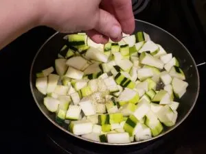 adding seasoning to zucchini in frying pan