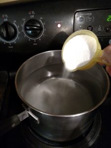 adding sugar to water in saucepan to make syrup for peaches.