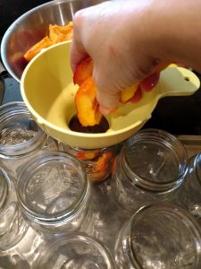 adding cut peaches to jars through funnel.