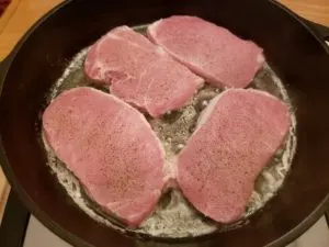 4 raw pork chops in skillet