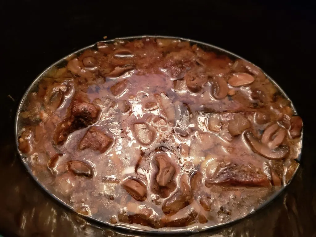 crock pot with broth, mushrooms, beef and onions after cooking