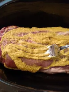spreading mustard over the roast with the back of a fork