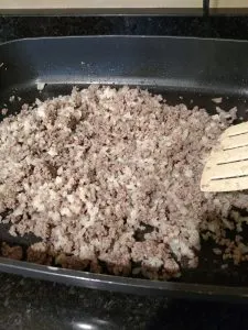 ground beef cooking in large electric skillet and stirring with spatula