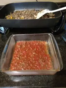 sauce in glass dish in front of electric skillet holding meat and vegetables