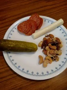 mixed nuts, string cheese, pepperoni and pickle on plate.