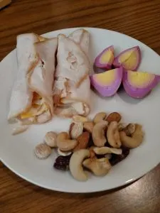 lunchmeat turkey and cheese rolled together, red beet egg quartered and mixed nuts on plate. 