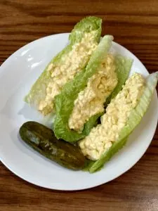 egg salad on lettuce leaves with a pickle on the side.