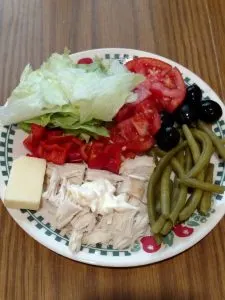 lettuce, tomato, black olives, pickled green beans, chicken and cheese on plate.