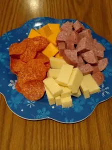 white and orange cheese cubed, cubed salami and pepperoni slices on blue plate