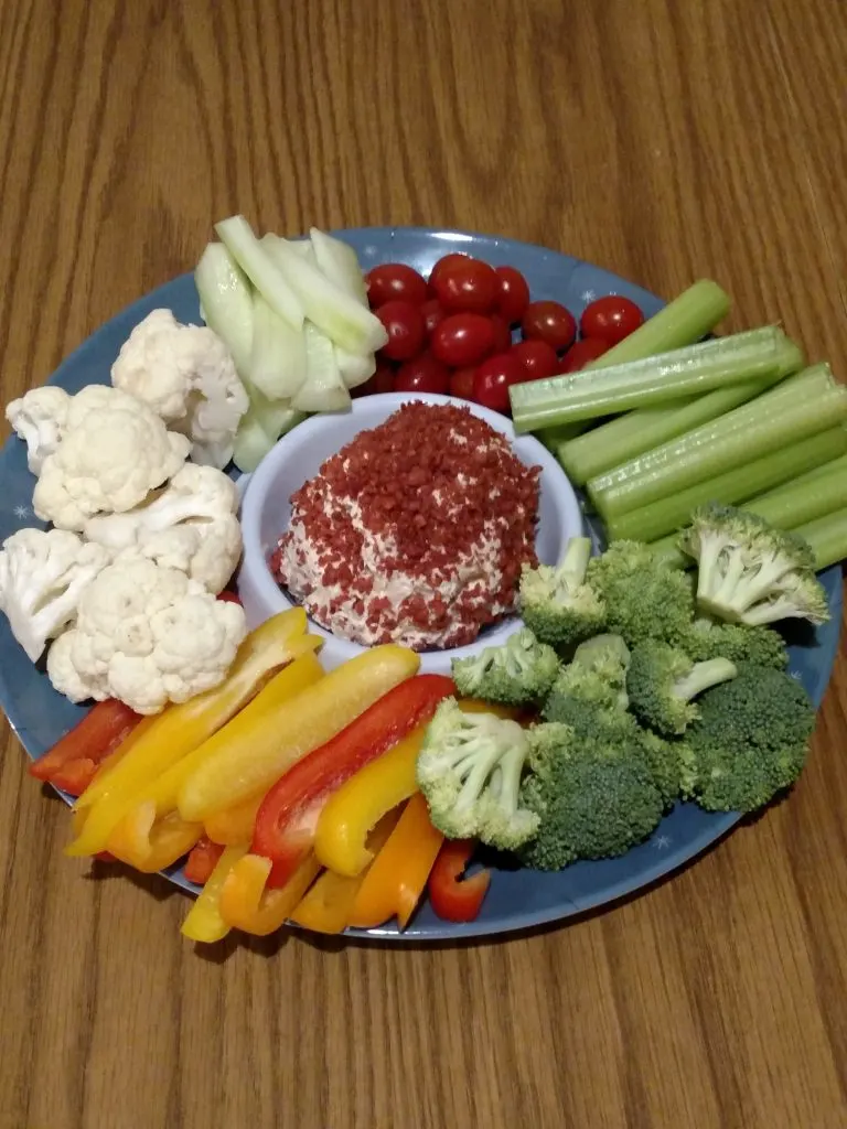 broccoli, cauliflower, colored peppers, celery, cucumbers and cherry tomatoes around edges and cheese ball in middle served on blue tray