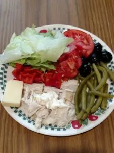 lettuce, tomato, black olives, pickled green beans, chicken and block of cheese on plate