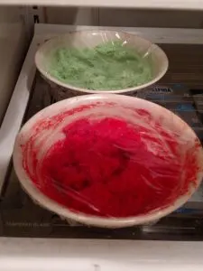 red and green bowls in refrigerator with plastic wrap over top.
