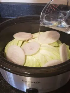 cabbage and onion in crock pot and pouring water over