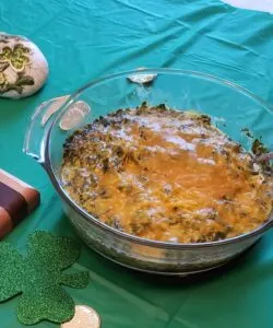 creamy spinach cheese bake with cheddar cheese on top in glass bowl on green table cloth