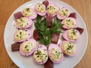 Deviled Red Beet Eggs on white plate with parsley sprigs in the center and pieces of beets around