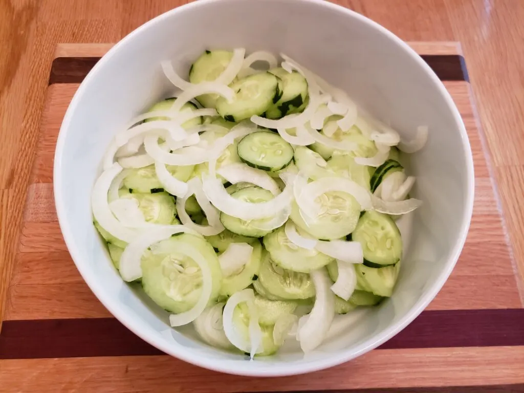 sliced cucumbers and onions in white bowl