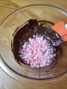 melted chocolate and oil mixture with crushed mints dumped on top in mixing bowl