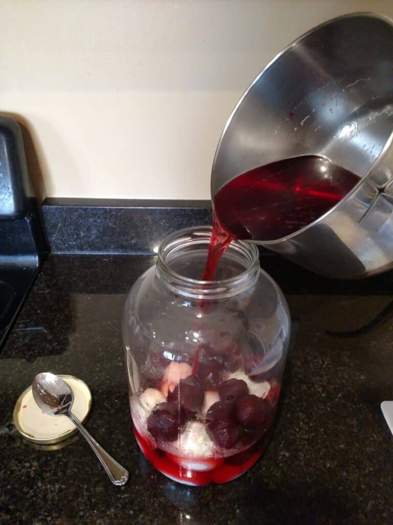 adding beet juice and vinegar mixture to glass jar of hardboiled eggs and beets