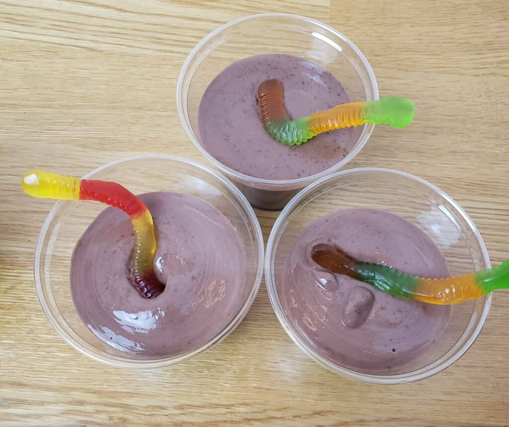 chocolate pudding in 3 plastic cups with 1 gummy worm in each