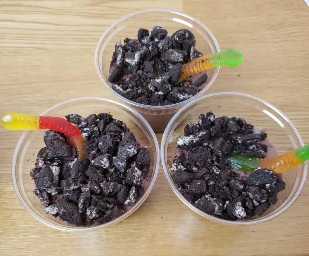 chocolate pudding in 3 plastic cups with 1 gummy worm in each and crushed Oreos on top