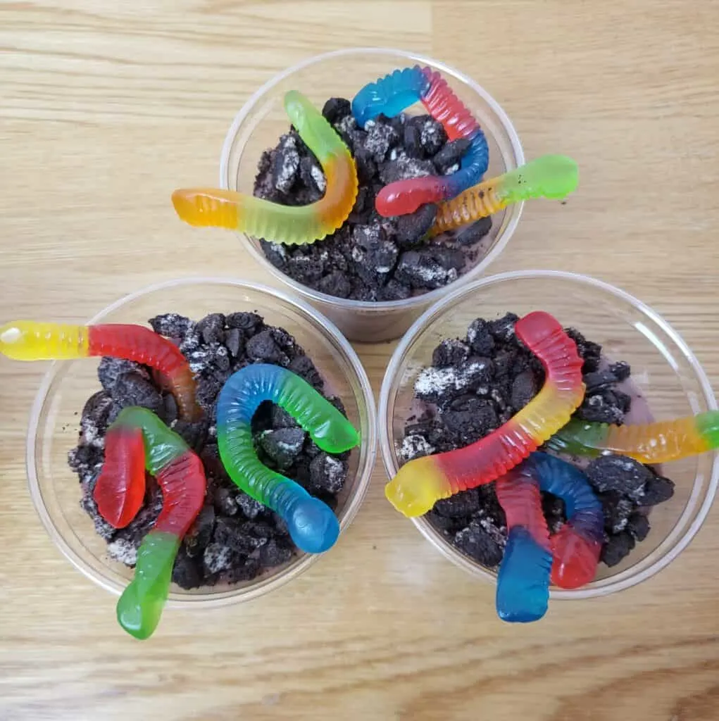chocolate pudding in 3 plastic cups with 3 gummy worms in each and crushed Oreos on top