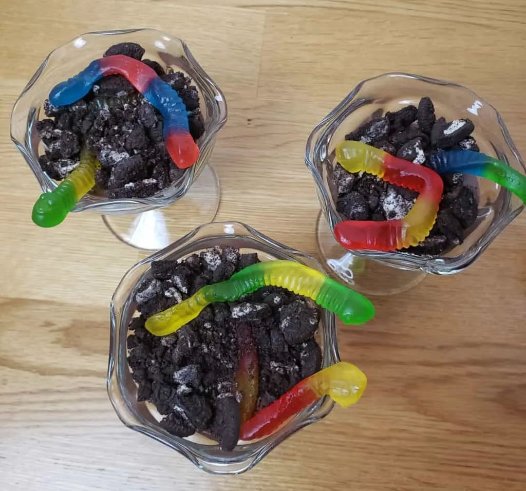 chocolate pudding in 3 plastic cups with 3 gummy worms in each and crushed Oreos on top