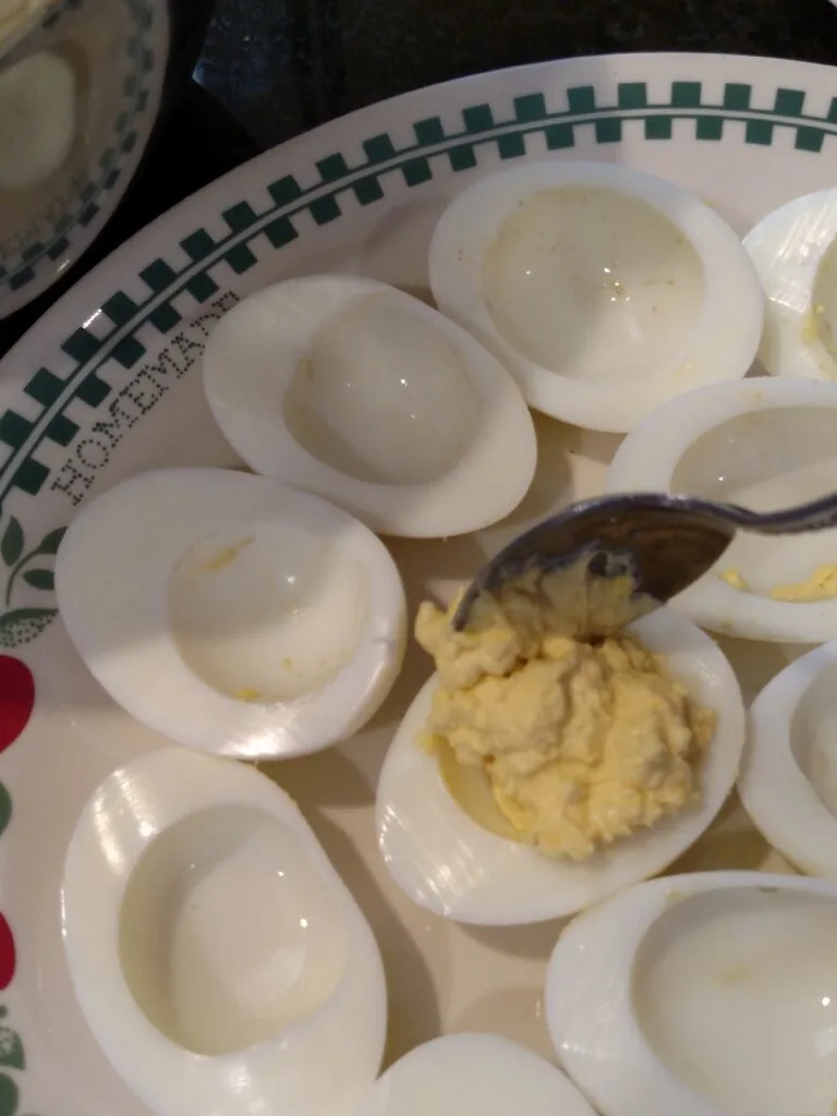 scooping deviled egg mixture into white of egg.
