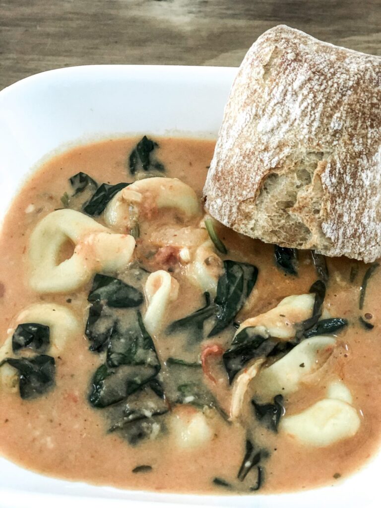 spinach tortellini soup in white bowl and bread on rim