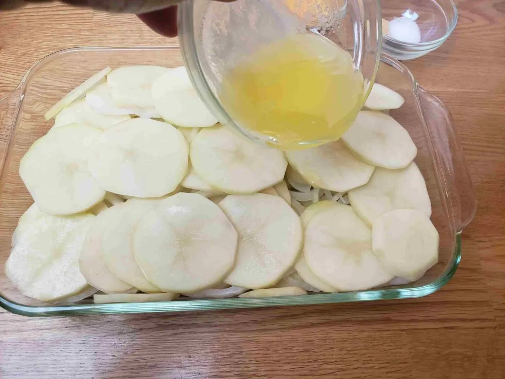 pouring melted butter over sliced potatoes and onions