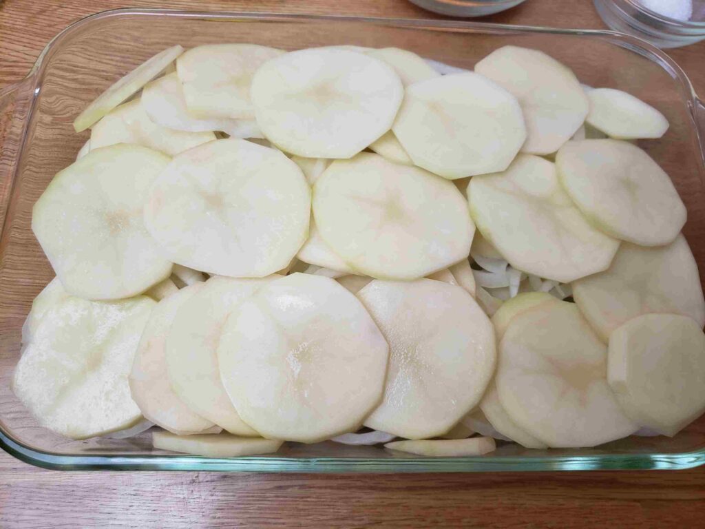 sliced onions and potatoes in glass baking dish