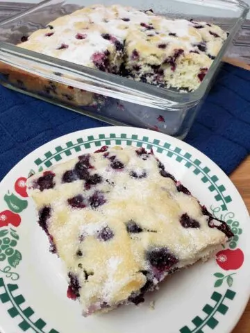 Overnight Blueberry Coffee Cake with a piece on plate in front of baking dish