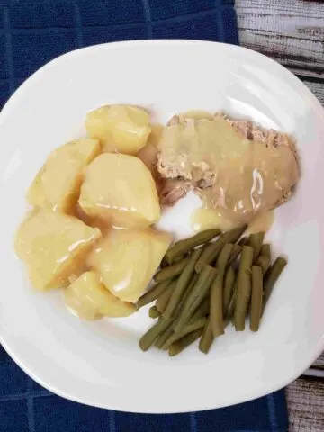 pork and potatoes with gravy and green beans on white plate